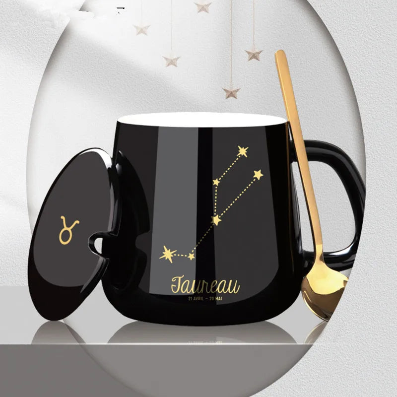 Black mug with Taurean constellation design and gold spoon on a light gray background