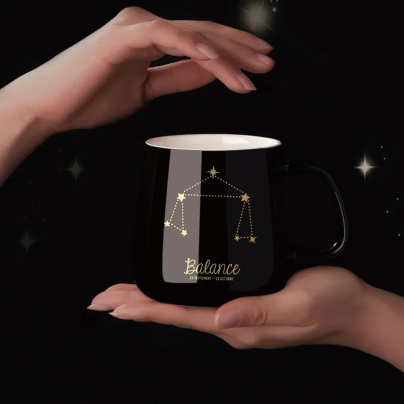 Black mug with 'Balance' zodiac design held between two hands against a dark background