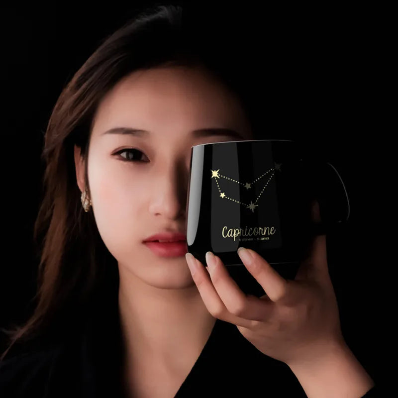 Woman holding a black mug with Capricorn zodiac design against a dark background