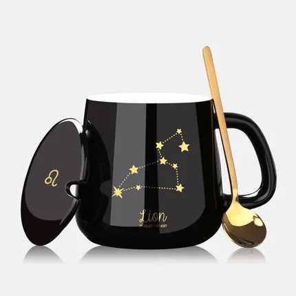 Black mug with gold constellation design, lid, and spoon on a light gray background