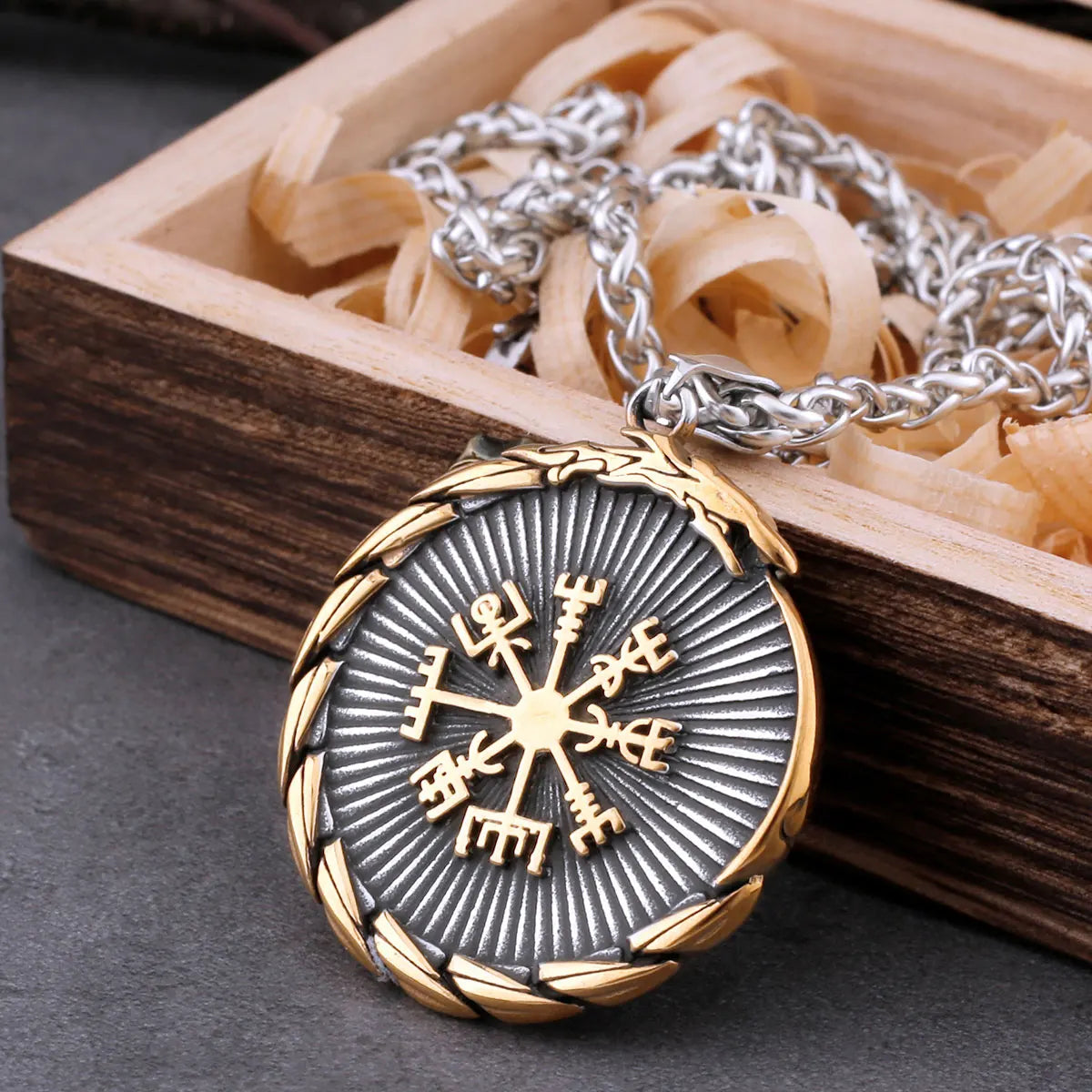 Viking compass pendant with gold and silver chain on a wooden box background