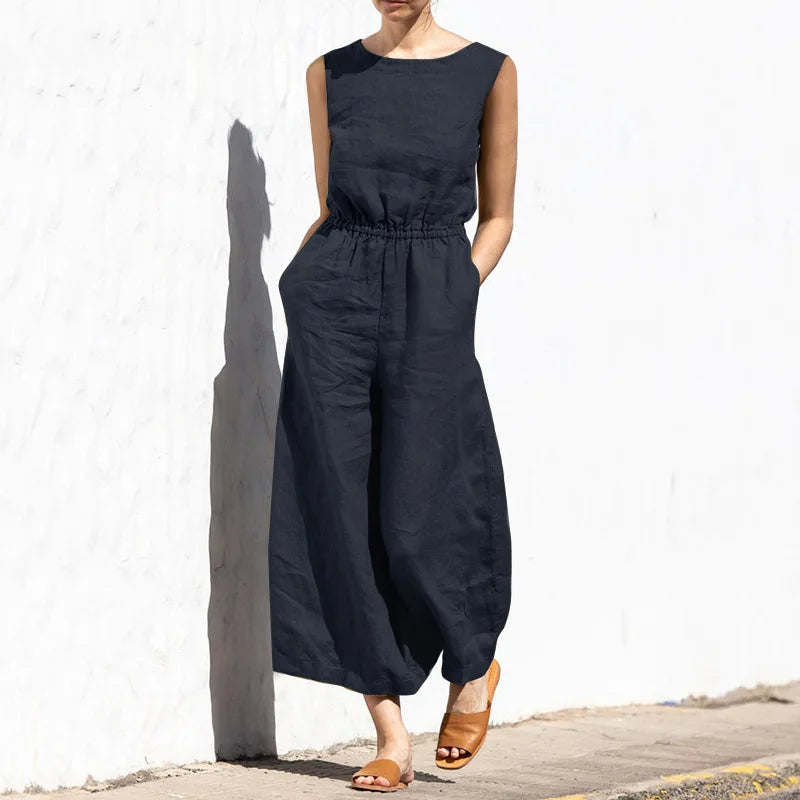 Person wearing a black sleeveless jumpsuit against a white wall.