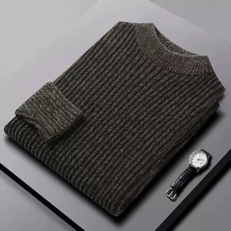 Folded gray sweater on a gray surface with a watch beside it