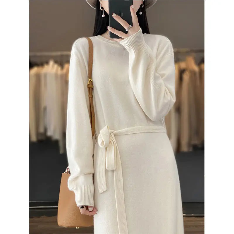 Person wearing a white dress with a belt, holding a brown handbag in a clothing store.