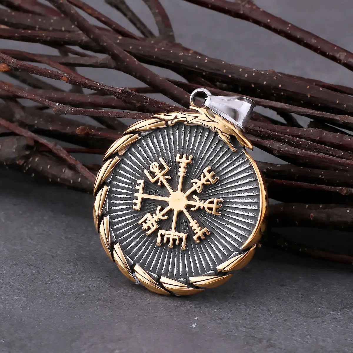 Viking compass pendant with gold and silver detailing on a dark surface with branches.