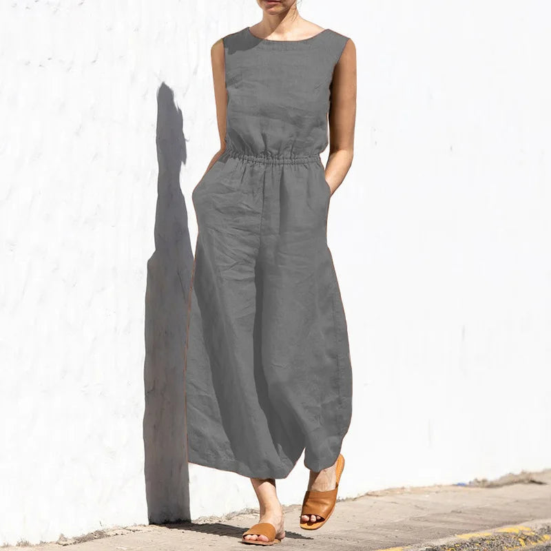 Person wearing a gray sleeveless dress against a white wall.