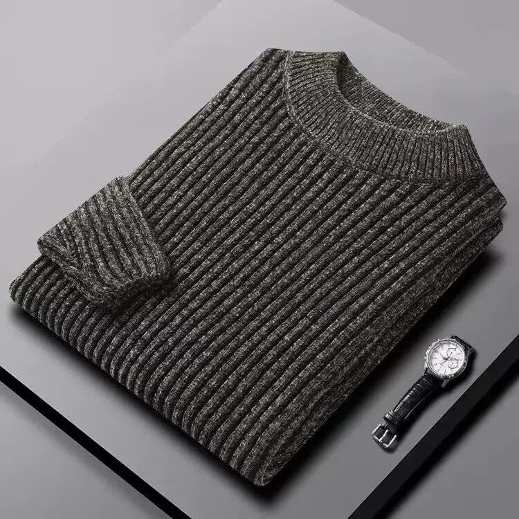 Folded gray sweater on a light gray surface with a watch beside it